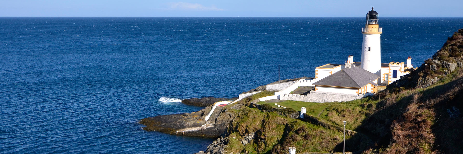 a white lighthouse is located a hillside