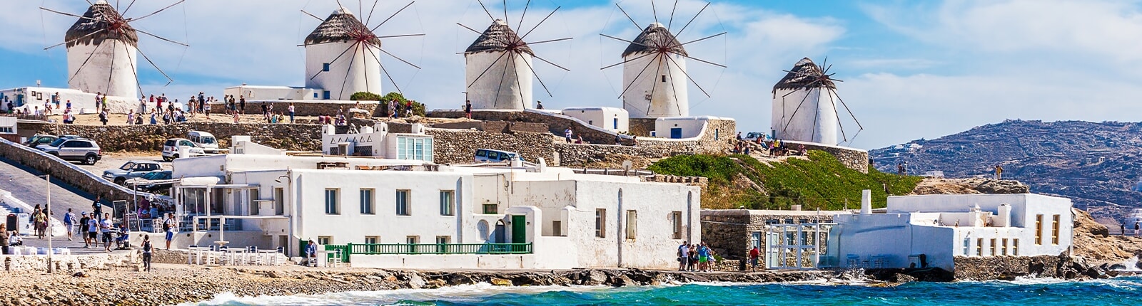 windmills lining mykonos streets with beautiful teal waters