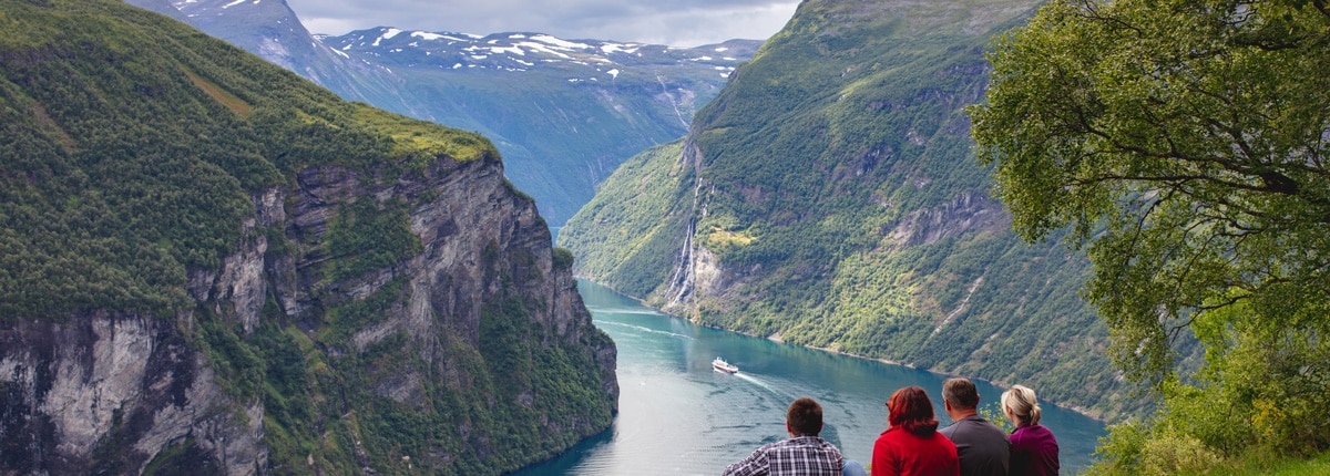 a family of four watches a boat sail along a fjord surrounded by mountains