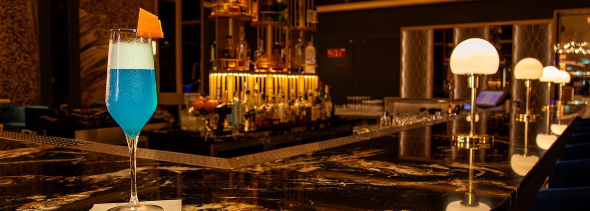 a tall blue drink on top of the golden mermaid bar counter