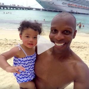 Man holding his daughter taking a selfie on the beach in front of Carnival cruise ship, link to Youtube video
