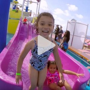 little girl smiles as she gets up from waterslide on a Carnival cruise ship, link to Youtube video