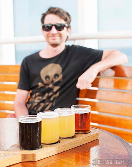 Four beer samples on a wooden holder with Randy in the background