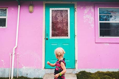 Young girl standing in front of a pink building with green door
