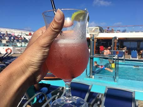 Hand holding up a pink margarita with a pool behind on the Carnival Conquest