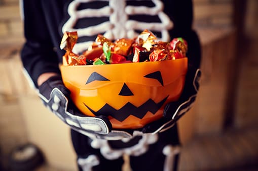 young boy in a skeleton costume holding bowl full of candy