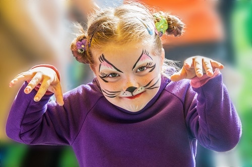 little girl paints her face to look like a cat during halloween 