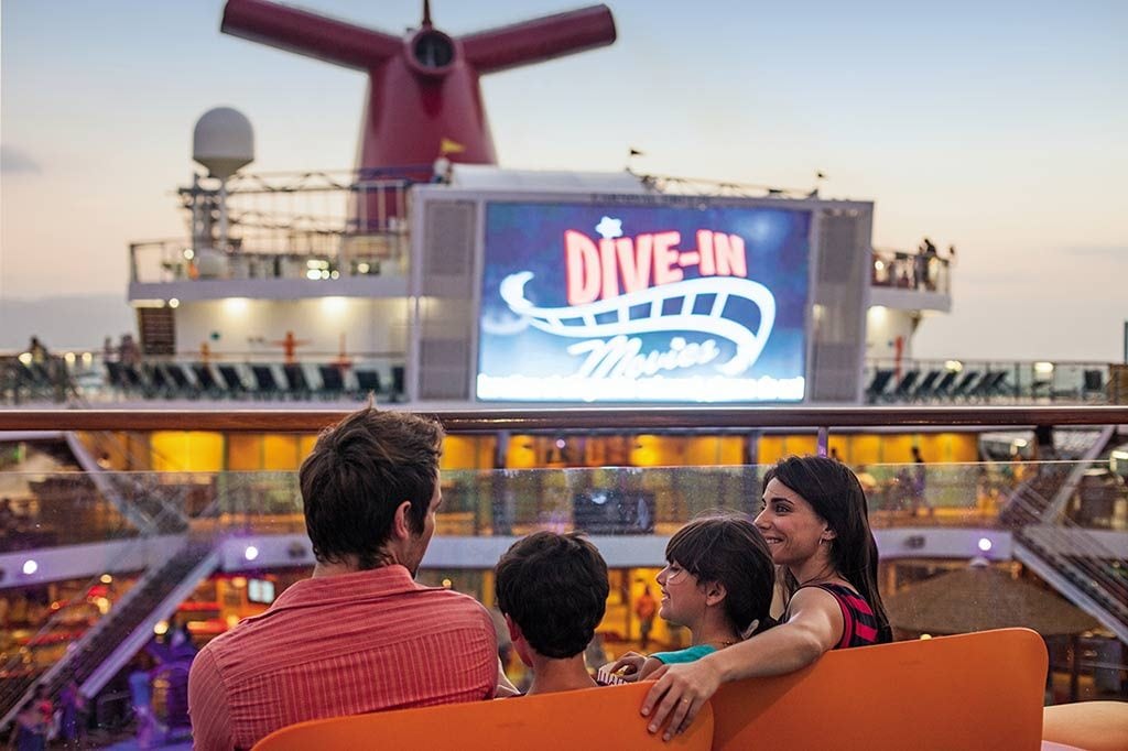 family sits on a carnival cruise deck and enjoys watching the seaside theater