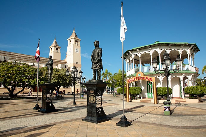 two statues with st philip the apostle cathedral in the background in parque central, puerto plata