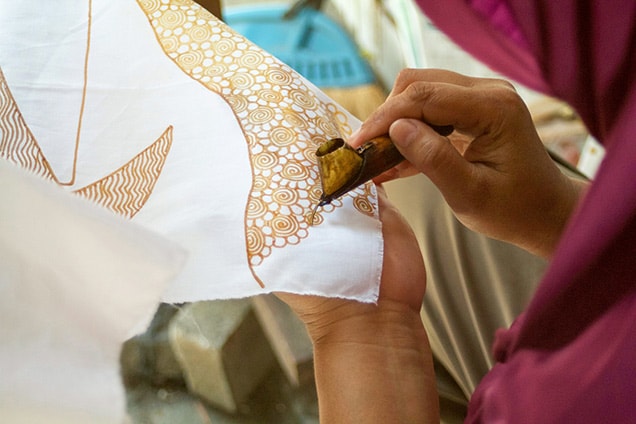 woman adding batik designs on a piece of white fabric