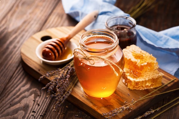 golden honey in a glass jar next to a honey dipper and honeycombs