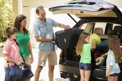 family of 5 putting their suitcases in a black minivan as they prepare to get on a cruise to hawaii