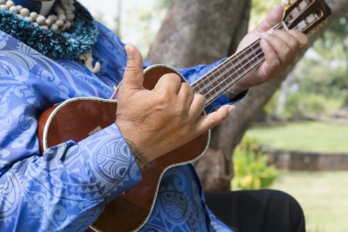 hawaiian man holding a ukulele as he shows the shaka sign