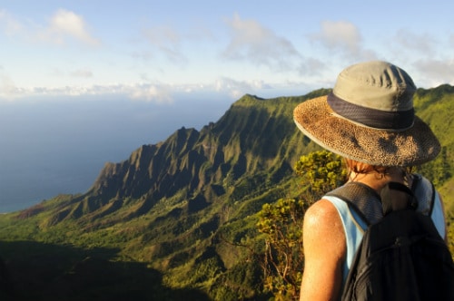 woman wearing a hat an backpack overlooking the waimea canyon in kauai hawaii