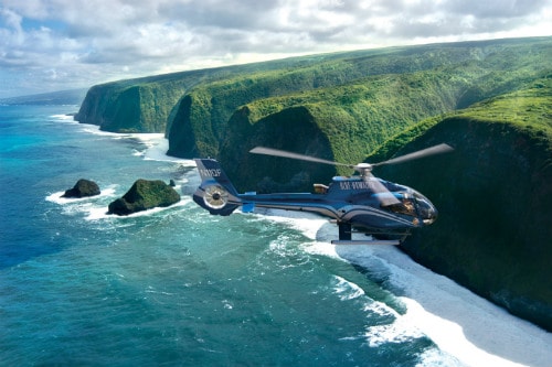 blue helicopter flying towards the lush big island of hawaii