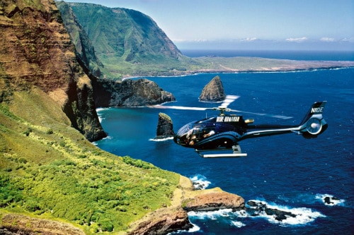 blue helicopter flying towards the green island of maui