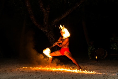 man with no shirt and a fire stick dancing a traditional hawaiian luau 