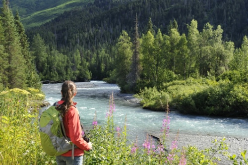 woman wearing a red jacket, hiking near a river in the alaskan forest