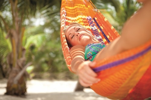 woman relaxing on an orange hammock during her stay in an oceanfront cabana 