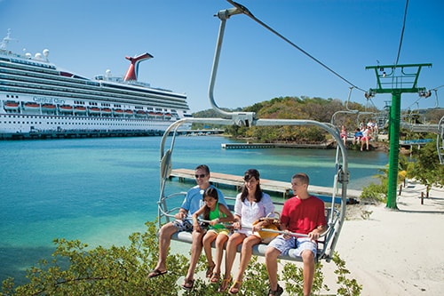 family of 4 going up a chair lift in the caribbean with carnival glory in the background 