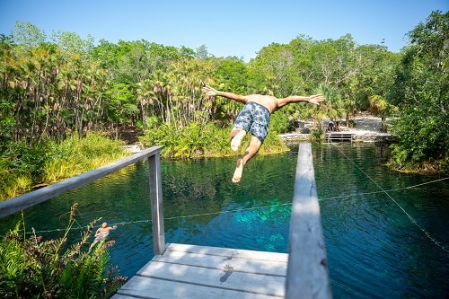 man diving off a wooden board towards a cenote in mexico 