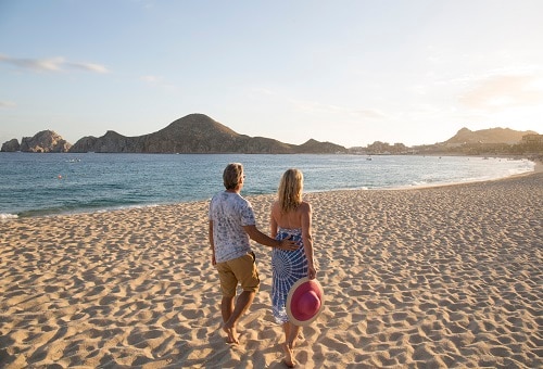 couple walking along the gorgeous beach of cabo san lucas as the sun sets