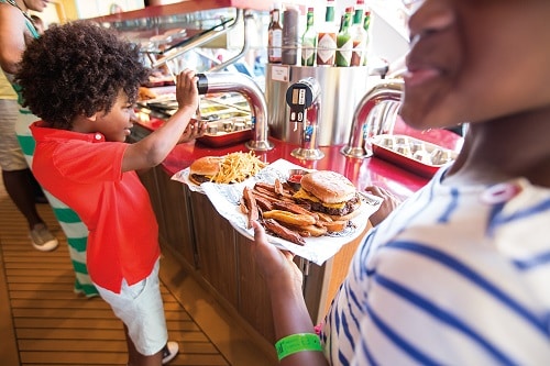 boy adding ketchup to his hamburger from guys burger joint on carnival breeze 