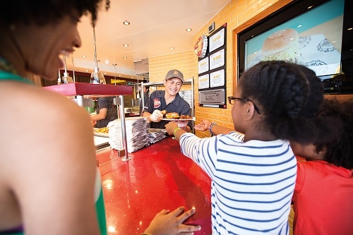 girl receiving burger and fries from guy’s burger joint on carnival spirit