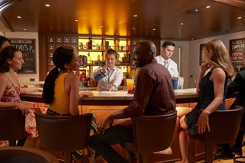 guest having a good time at the alchemy bar onboard carnival vista as a bartender serves a cocktail