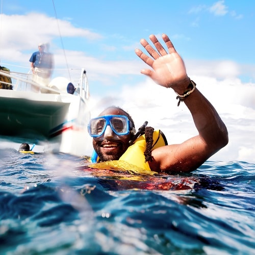 man waving at the camera as he snorkels in the caribbean sea