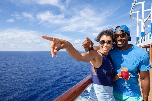 couple wearing sunglasses and holding a cocktail, pointing at a hawaiian island 