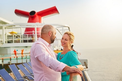 couple standing together at the railing by the funnel onboard a carnival ship