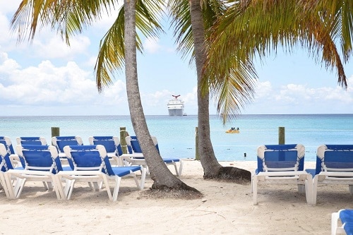 a carnival ship pulling up to a beach with palm trees and chairs in princess cays