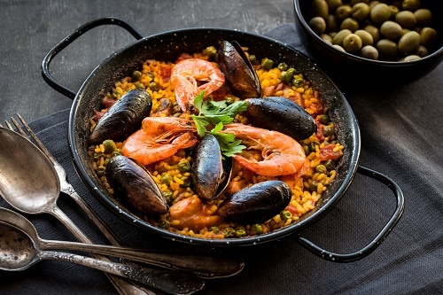a black paella pan with fresh seafood paella served on it