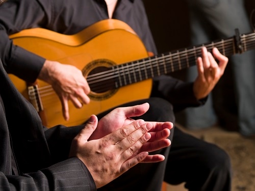 a man playing flamenco music on a guitar while another man claps along