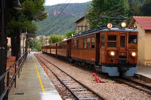 a vintage train passing through a station in the town of soller