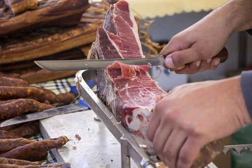 butcher cutting up prosciutto in a marketplace