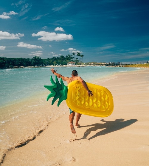 man carrying a pineapple floaty to the beach in nassau