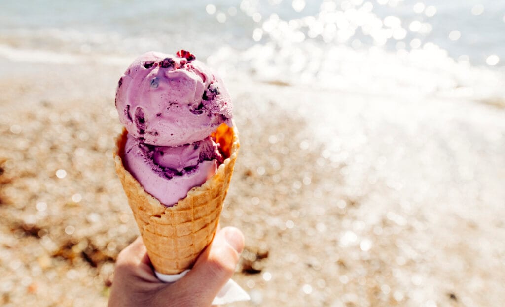 Picture of a holding a cone of exotic purple ice cream on a beach.