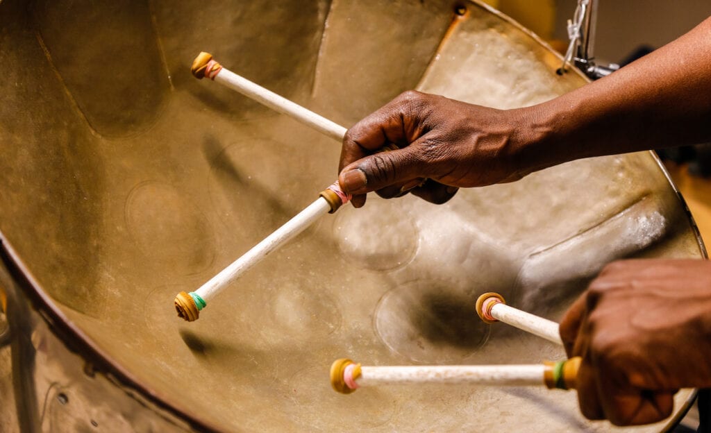 Closeup image of the hands of someone playing steel drums.