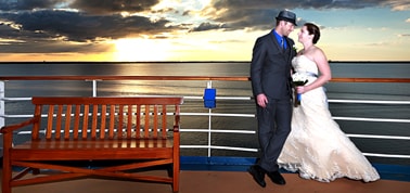 a newlywed couple posing for photos after their wedding on a carnival cruise with the sun setting in the background