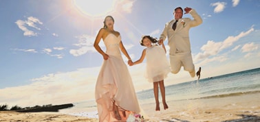 a couple and their daughter jumping after a wedding ceremony on a beach